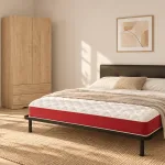Dormitorio amueblado con cama de cabecero tapizado, colchón con banda roja y armario de madera